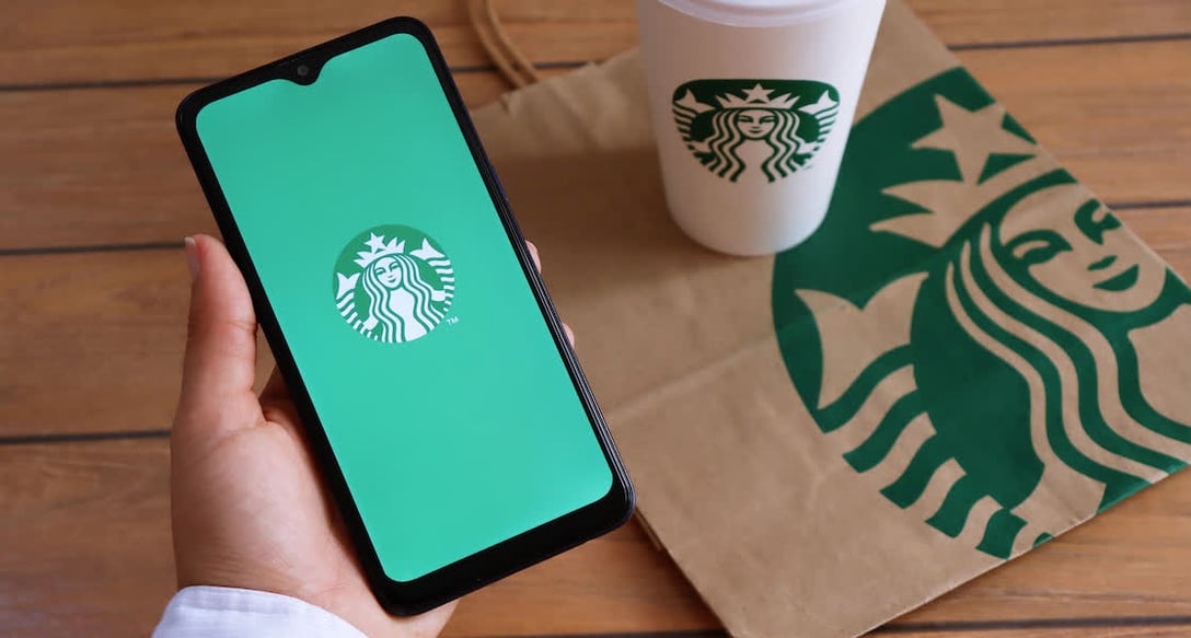 A picture of a Starbucks coffee and someone holding their phone with the Starbucks logo on the screen.
